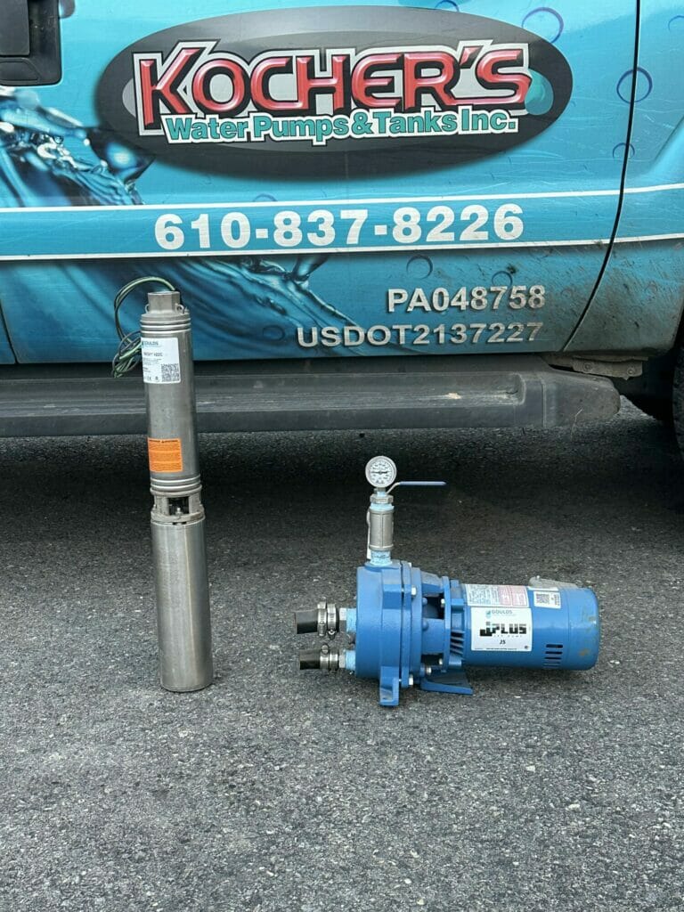 A water well pump and a blue water pressure booster are displayed on the ground, with the blue van of 'Kocher's Water Pumps & Tanks Inc.' in the background, including their contact number and other details.