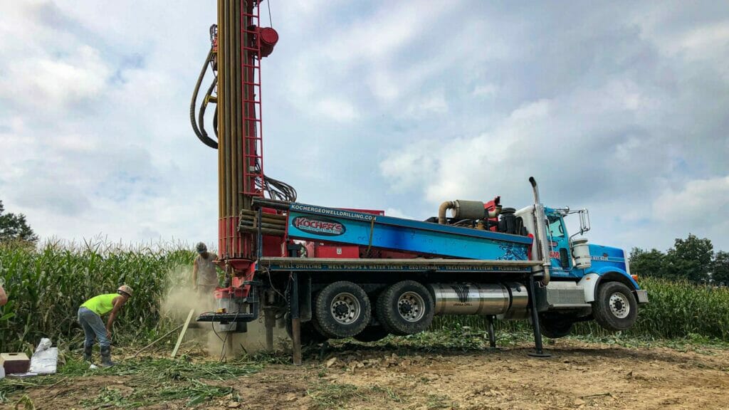 Kocher's drill rig mounted on a truck, with an employee initiating the well-drilling process in a cornfield.