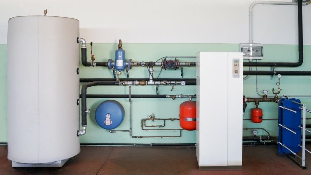 A geothermal heating and cooling system setup with various connected pipes, pressure gauges, and a large water storage tank, showcasing a renewable energy solution.