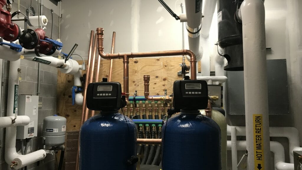 Interior of a well water filtration system room with blue pressure tanks, copper piping, and valves indicating a complex residential water treatment setup